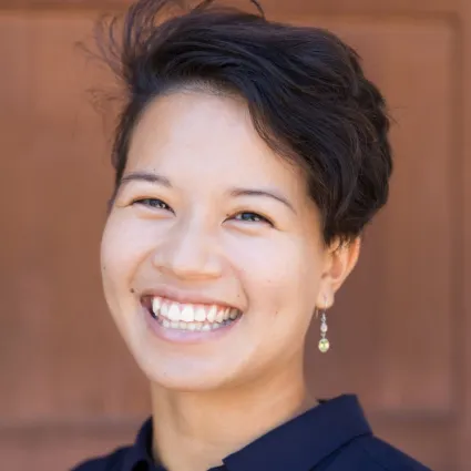 Headshot of Genae Matthews smiling cheerfully, wearing a dark collared shirt and drop earrings.