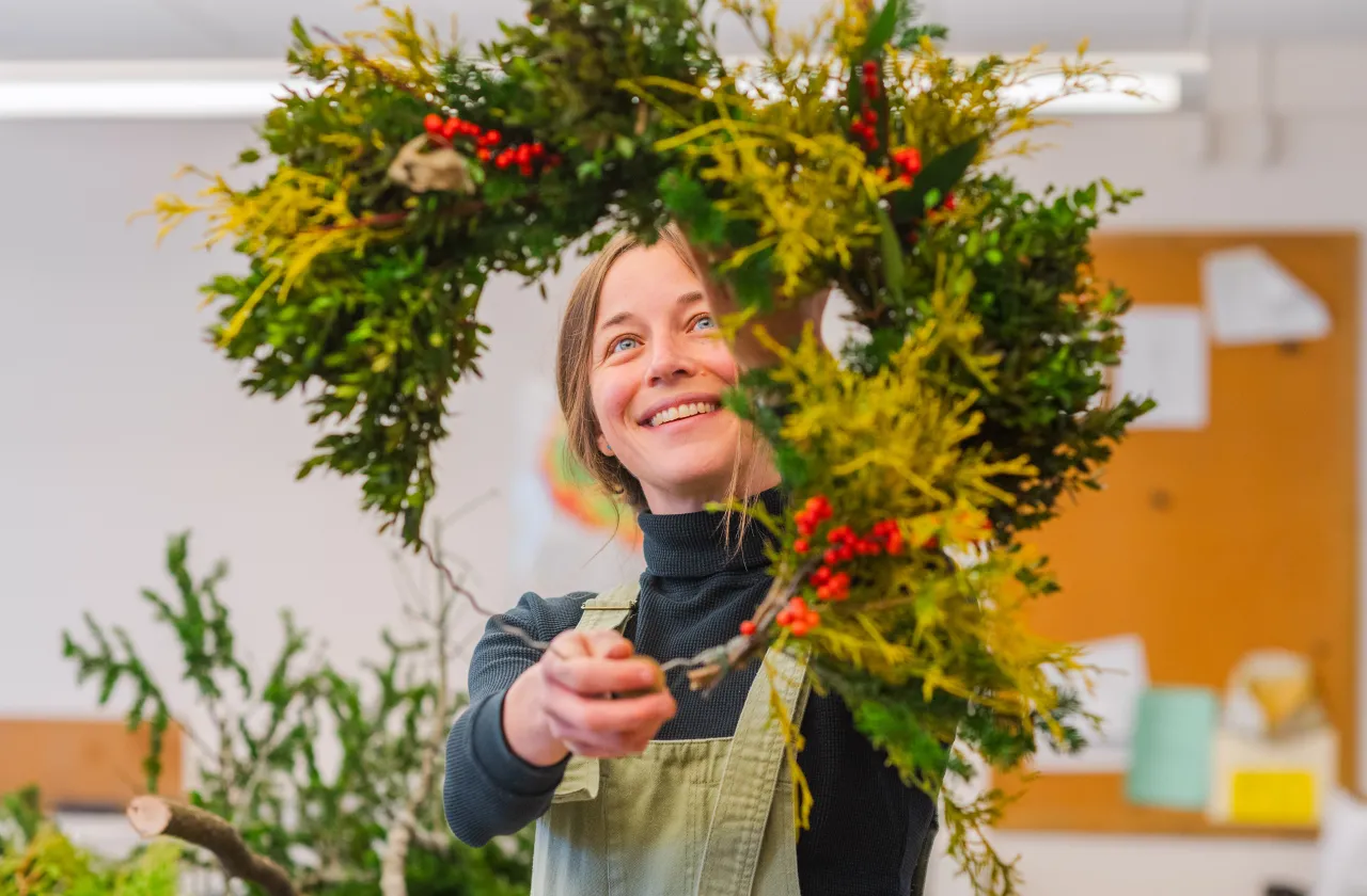 Julie Thomson smiles while holding a half completed wreath