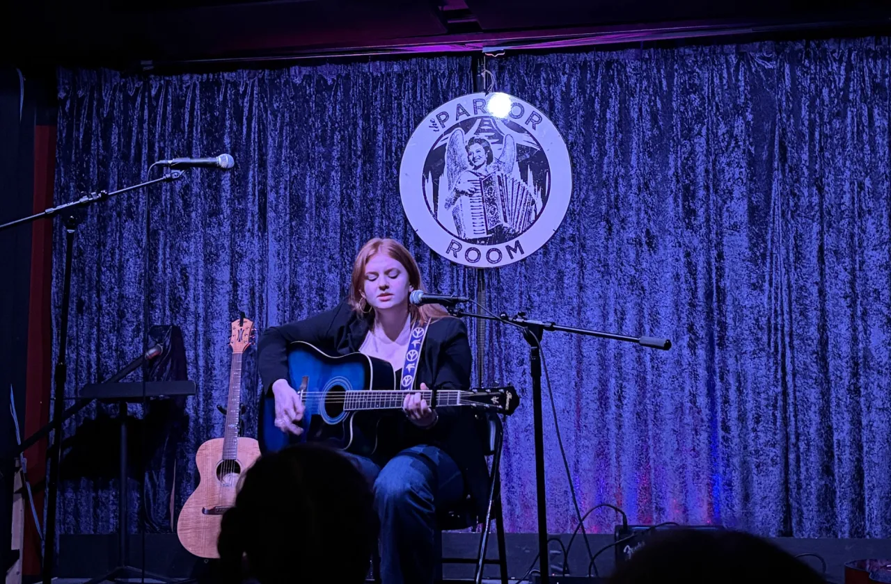 A student on stage with an acoustic guitar and a microphone