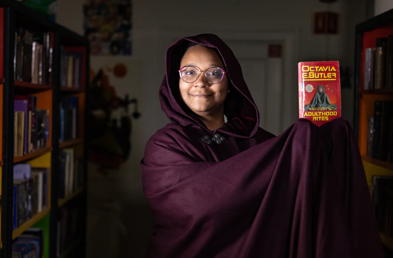 Anne-Marie Martin '26 wears a dark cloak while holding up a copy of Adulthood Rites by Octavia Butler.