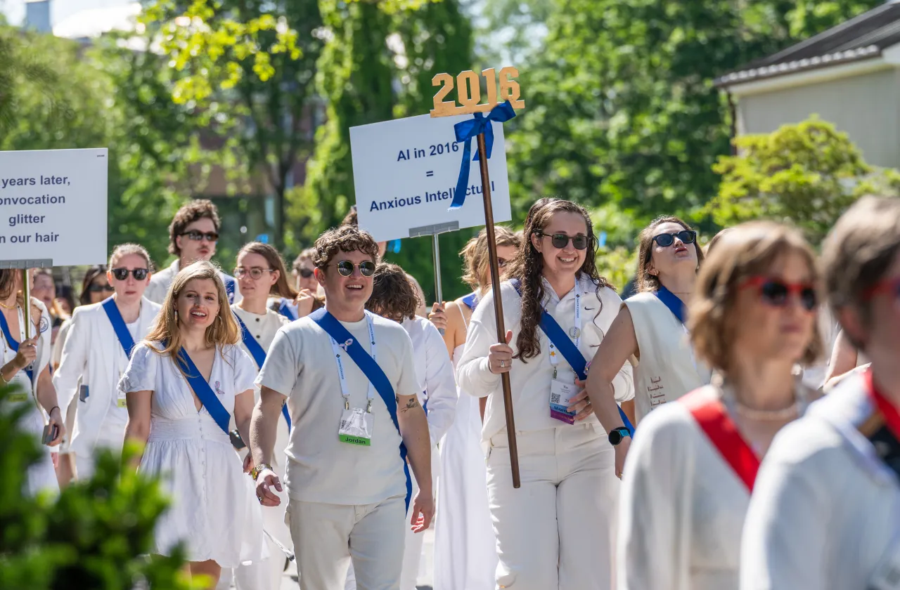 Members of the class of 2016 march in the Alum Parade, wearing white and blue sashes.