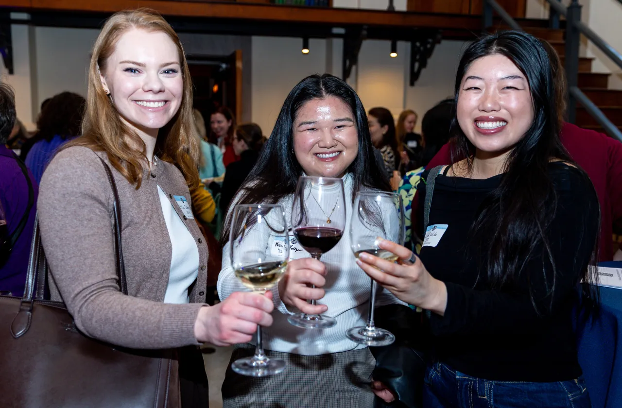 Three young alums smiling while toasting the camera