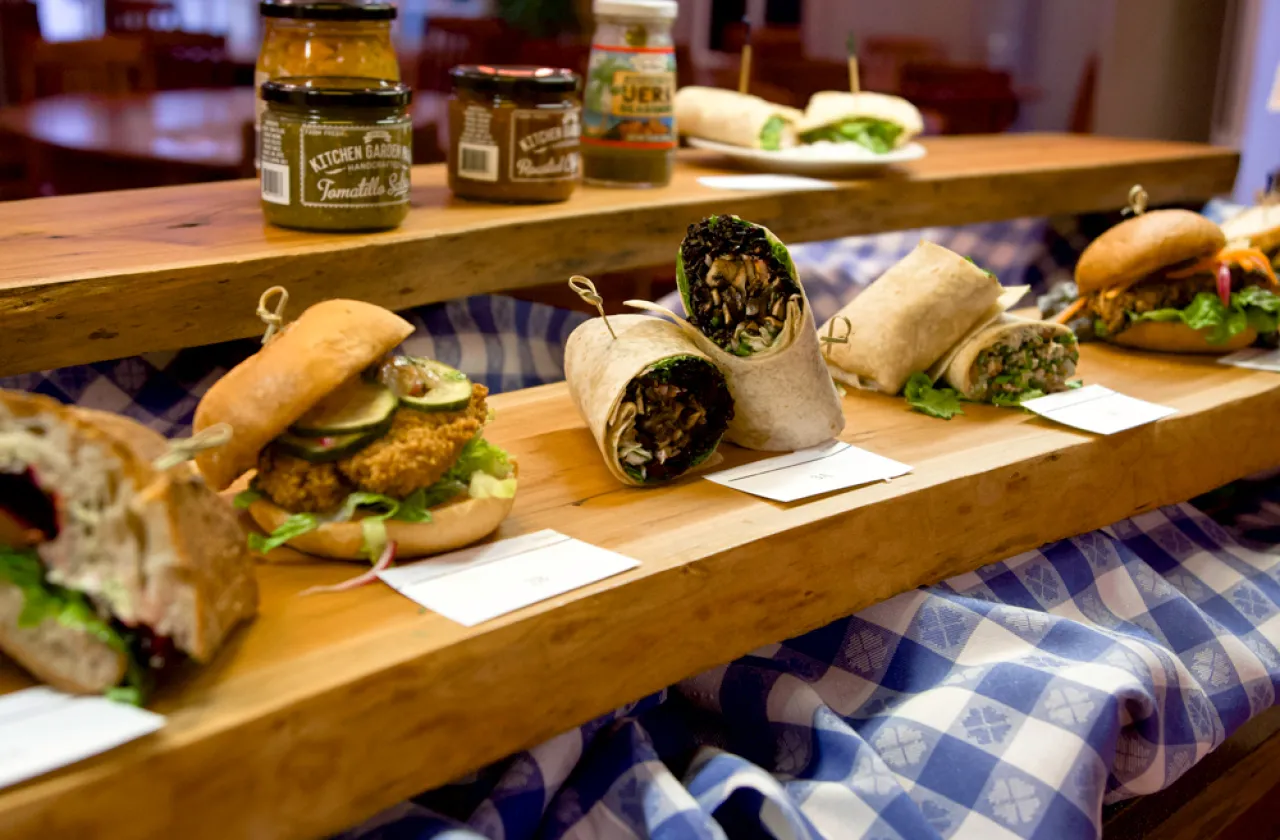 Row of sandwiches and wraps on a wood shelf with condiments on another shelf behind and above