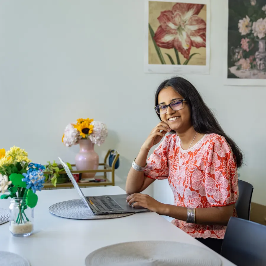 Sirohi Kumar smiles while sitting at a table with her laptop.