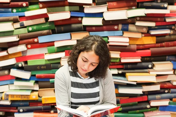Student reading a book in front of piles of differently colored books