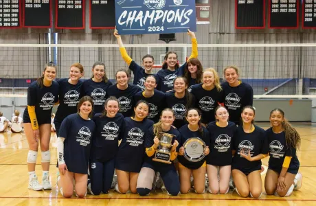 The volleyball team posing with their NEWMAC championship banner