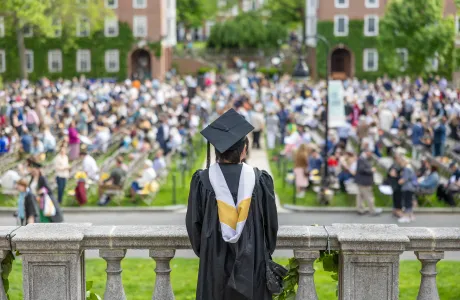 A senior in cap and gown faces away from the camera, looking out into the Quad on Commencement Day