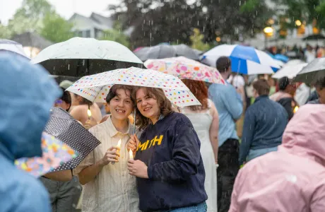 A senior and a guest stand underneath a polka-dotted umbrella in the rain during Illuminations