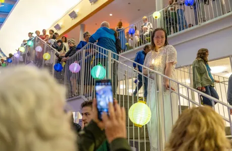 A senior holds an electronic candle, smiling on the interior steps of the Campus Center, admiring the lanterns during Illunminations