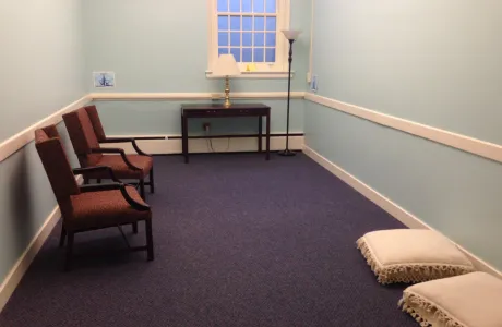 The blue room in the chapel, featuring chairs and cushions, lamps, and signage on the walls noting direction.