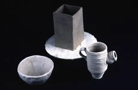 Ceramic art pieces, including a square vessel on a circular slab, a simple bowl, and a textured mug with a handle