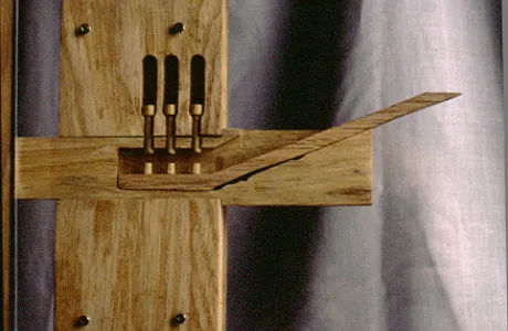 A wooden mechanical sculpture features vertical bars and a long lever