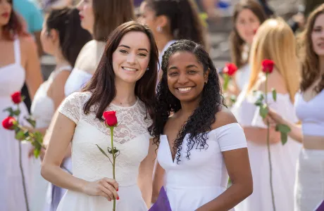 Two students in white Ivy Day dresses holding red roses