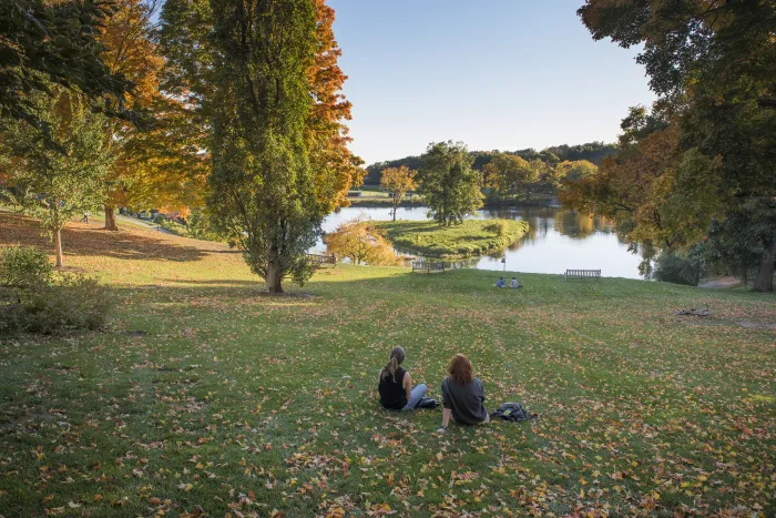 Two students sitting in front of Paradise Pond in the fall.