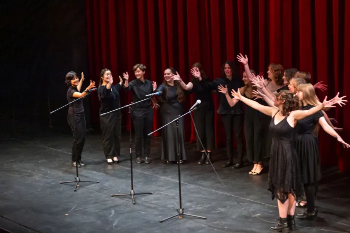 Students performing on stage, their hands and arms raised.