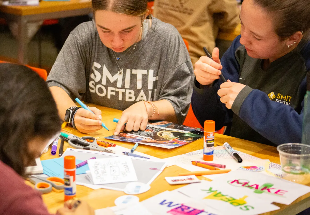 Two students lean over a table with markers while creating a zine at ZineFest