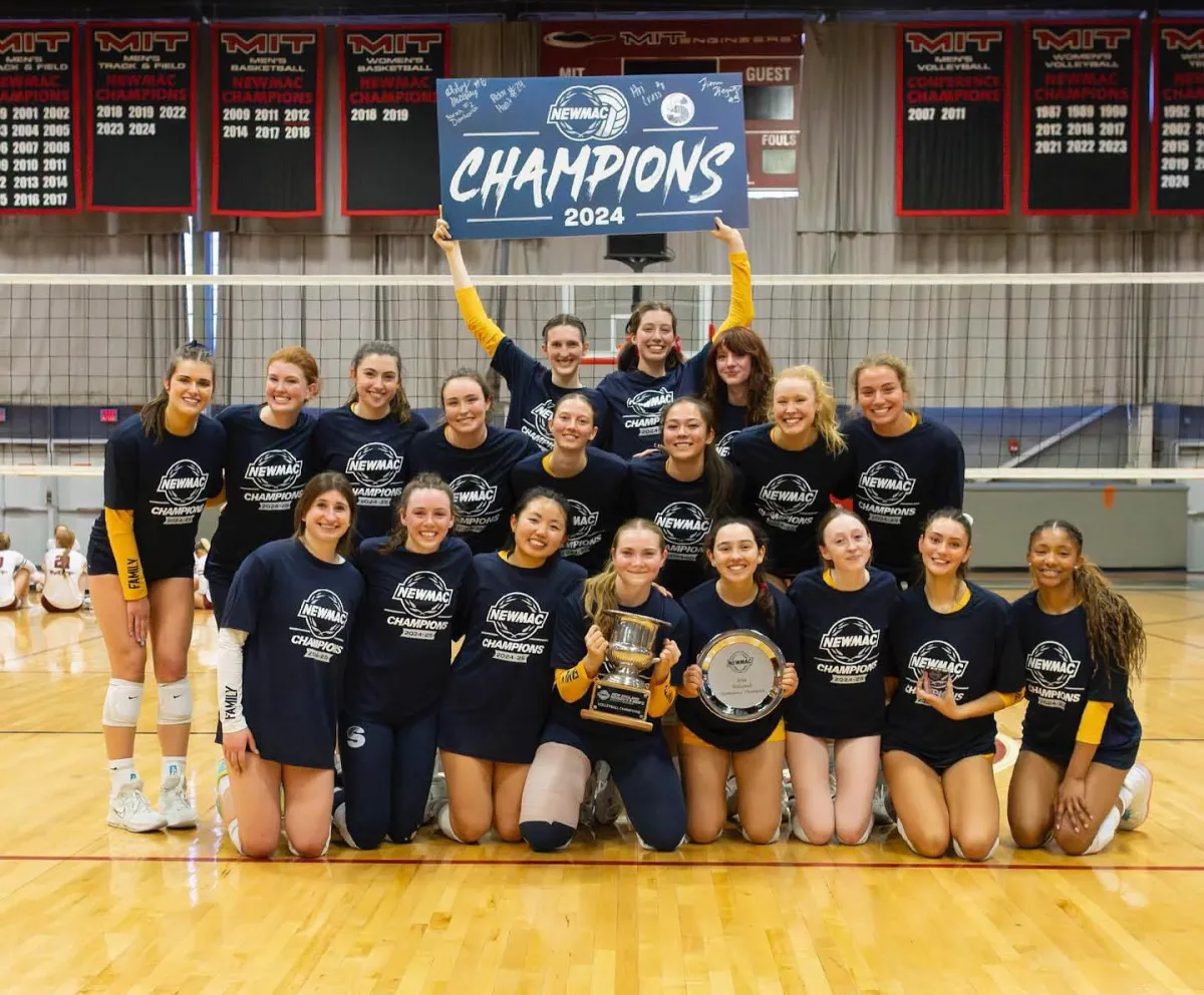The volleyball team posing with their NEWMAC championship banner