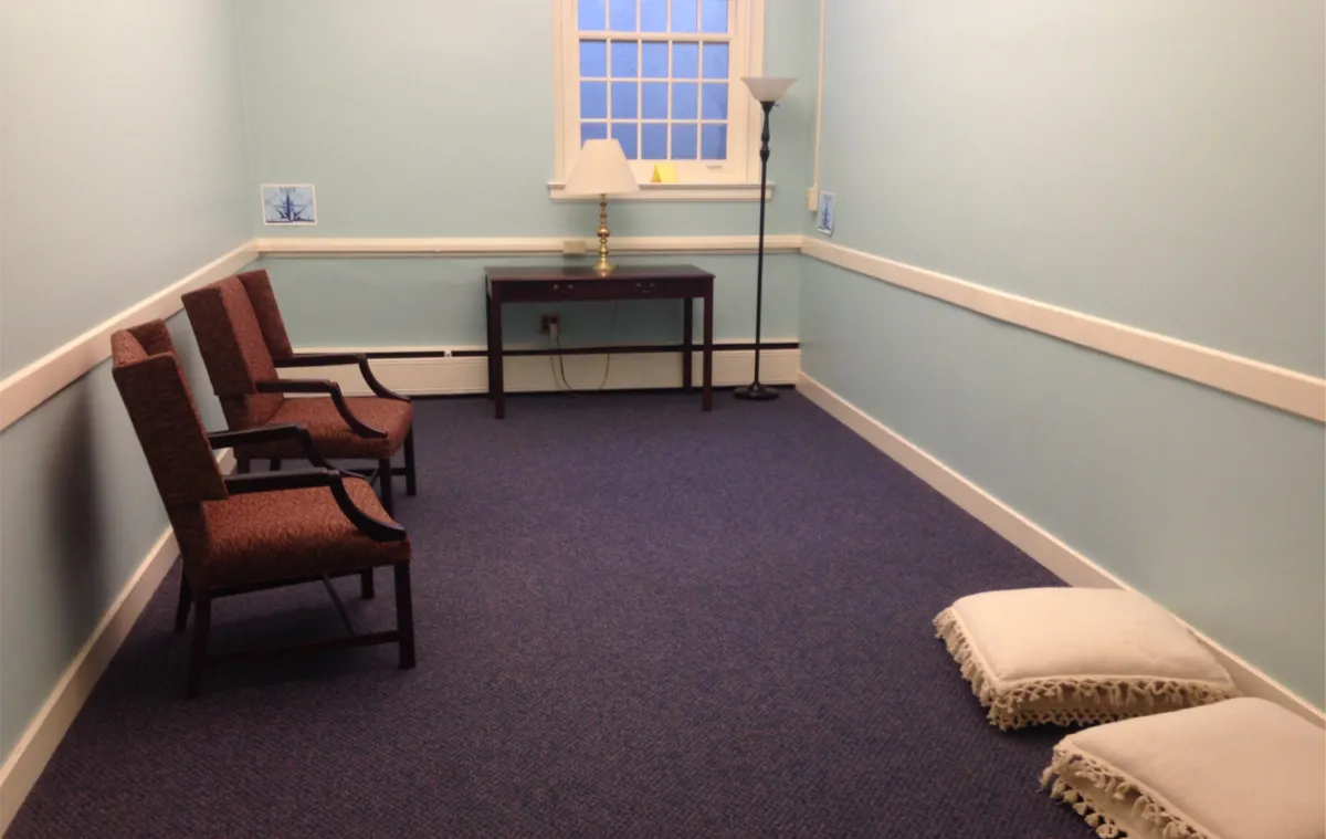 The blue room in the chapel, featuring chairs and cushions, lamps, and signage on the walls noting direction.