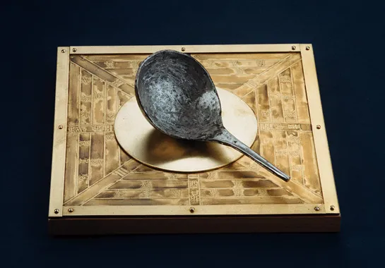 Ancient Chinese compass with a spoon-shaped lodestone on a bronze plate, depicting traditional Chinese symbols