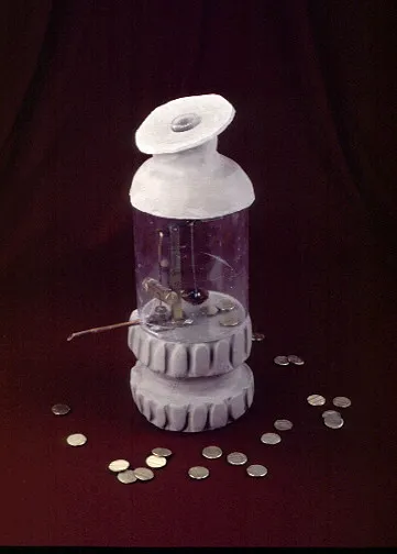 A small sculpture resembling a bottle rocket has a white top, a transparent middle, and coins scattered around its base