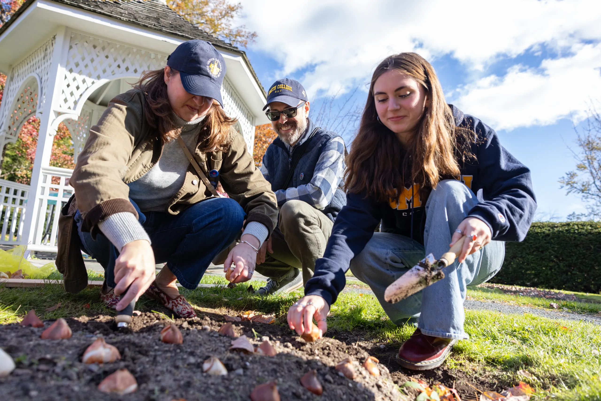 A student and parents plant garlic bulbs near the Capen gazebo