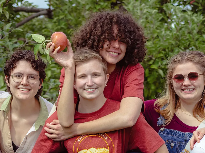 One student giving another a piggy back ride while they hold an apple
