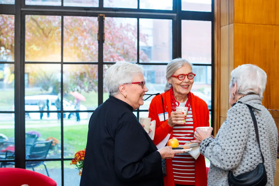 Three alums gathered in the Alumnae House smiling and talking.