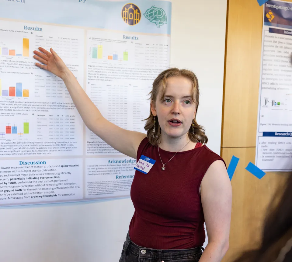 Hannah Hafner stands in front of her poster for Collaborations, speaking to an onlooker