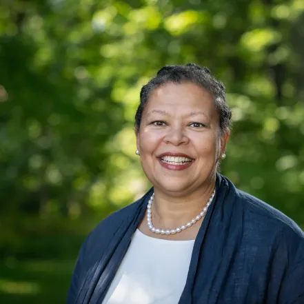 Photo of Sarah Willie-LeBreton smiling outdoors, in front of a background of green trees